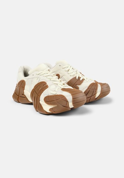 Stevige gebroken witte sneakers met dikke, gestructureerde bruine zolen, bovenwerk van mesh en leer, vetersluiting, naast elkaar getoond op een witte achtergrond.