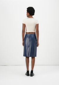 Marineblaue Lederrock mit einem Reißverschluss auf der Rückseite und einem Schlitz, kombiniert mit einem taillierten beigen Cropped-Top. Das Outfit wird mit schmalen, schwarzen Schuhen ergänzt.