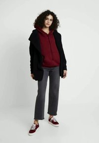 Cárdigan negro de gran tamaño, sudadera burdeos, pantalones rectos gris y zapatillas rojas con patrón y suelas blancas, con un corte relajado.