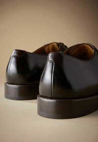 Zapatos de cuero negro con un acabado brillante, con una forma redondeada, tacón de altura media y una sutileza de costura a lo largo de la suela.