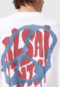 Hvit t-skjorte med et stort, abstrakt rødt og blått grafisk motiv som inkluderer et fredssymbol og et dryppende maleeffekt på baksiden.