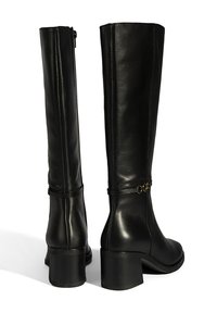 Bottes hautes jusqu'au genou en cuir noir avec un talon carré, dotées d'une fermeture éclair arrière et d'une chaîne décorative en cercle doré au niveau de la cheville.