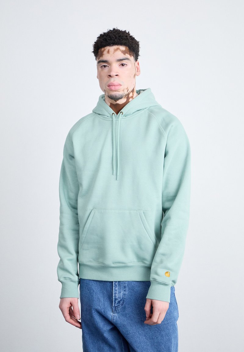 Hellgrüner Sweatshirt mit Kapuze, Kängurutasche und elastischen Bündchen. Hergestellt aus weichem Stoff, mit einem kleinen gelben Logo-Detail am Ärmel.