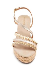 Sandale espadrille beige avec des lanières métalliques, des accents de perles décoratives et une semelle en jute tissée. Bride de cheville réglable pour un maintien sécurisé.