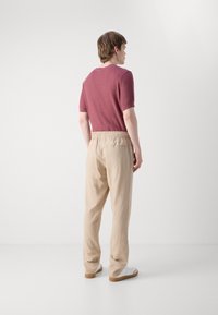 Kortermet, burgunder strikket skjorte kombinert med løse, beige bukser med elastisk midje, supplert med hvite sneakers.
