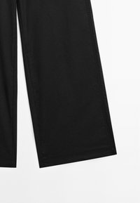 Pantalons noirs à jambes larges présentés sur fond blanc, avec une texture de tissu lisse et des coutures soigneusement finies.