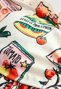 Färgglad badklädestyg med en tomatinspirerad tryck med olika konservburksdesigner, i huvudsak vit bakgrund, med volanger vid kanterna.