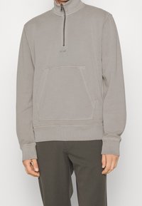 Felpa grigia con zip a quarto realizzata in tessuto morbido; presenta una tasca frontale, polsini a coste e un logo discreto sul petto.