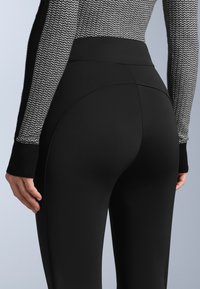 Černé legíny s vysokým pasem vyrobené z elastického materiálu, s přiléhavým střihem a hladkou strukturou, prezentované s texturovaným svetrem.