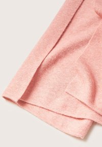 Tissu tricoté rose doux plié pour montrer la texture et les ourlets sur une surface plane et claire.