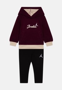 Felpa bordeaux con dettagli crema e logo Jordan, abbinata a leggings neri con logo bianco. Tessuto di cotone morbido e texture.