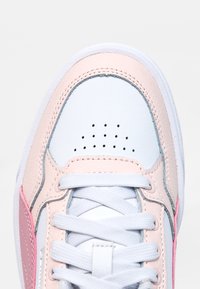 Weißer Sneaker-Zehenbereich mit hellrosa Akzenten, weißen Schnürsenkeln und perforierten Belüftungslöchern auf dem oberen Teil.