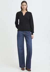 Czarny sweter z długim rękawem i dekoltem w serek, zestawiony z szerokimi, ciemnoniebieskimi jeansami. Do tego brązowe buty na platformie.