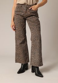 Pantalons à larges jambes en imprimé léopard marron et noir, en tissu doux, dotés de deux poches latérales et d'une taille haute. Stylés avec des bottines noires.