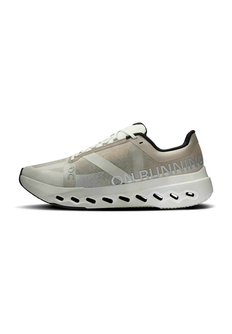 Chaussure de sport avec une tige en maille beige et grise, cordons blancs, un talon structuré et une semelle texturée avec des découpes pour le rembourrage.
