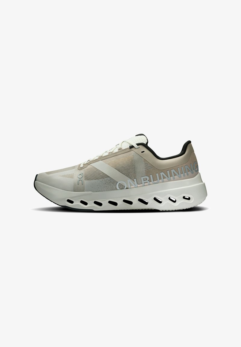 Chaussure de sport avec une tige en maille beige et grise, cordons blancs, un talon structuré et une semelle texturée avec des découpes pour le rembourrage.