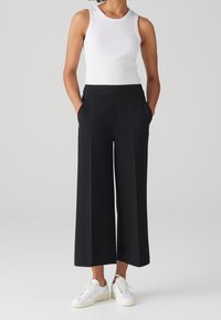 Pantalons larges noirs avec poches latérales, associés à un débardeur ajusté blanc et des baskets blanches. Tissu lisse et silhouette décontractée.