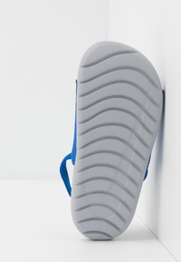 Modrá sandal s texturovanou šedou gumovou podrážkou. Podrážka má vlnkový vzor pro lepší přilnavost. Viditelný je také detail bočního popruhu, který je vyroben ze měkkého materiálu.