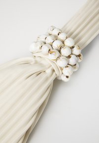 Tessuto beige plissettato con un accento di perle bianche. Le perle sono lucide con motivi marmorizzati, che aggiungono texture al design.