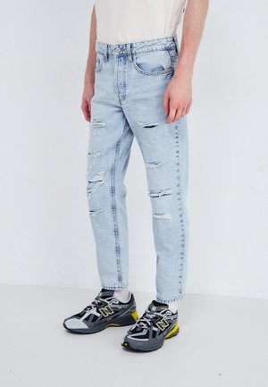 Lichtgewicht spijkerbroek van denim met versleten scheuren, recht gesneden pasvorm en een hoge taille. Gecombineerd met zwart en grijs sportschoenen met gele accenten.