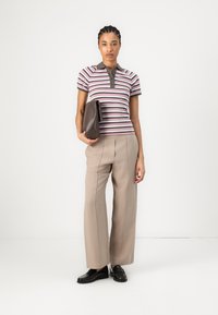 Randig pikétröja med krage, grå och rosa nyanser. Tillsammans med beige vida byxor och svarta loafers. Håller en brun kuvertväska.