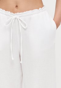 White textured pants with a gathered waistband and drawstring. Features side pockets and a relaxed fit. Light, breathable fabric.