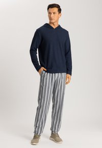 Sudadera con capucha en color navy y mangas largas, combinada con pantalones a rayas en gris y blanco. El modelo lleva puesta una zapatilla ligera gris.