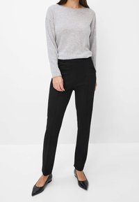 Haut gris à manches longues associé à un pantalon noir ajusté. Tissu lisse avec poches avant plates et coutures tailleur. Ballerines à bout pointu noires.