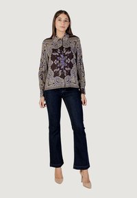 Blusa nera con motivo a paisley elaborato in blu e oro, chiusura frontale a bottoni, maniche lunghe, abbinata a jeans di denim scuro.