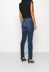 Siniset farkut slim fit -mallilla, joissa on takataskut ja huomaamaton tikkaus. Yhdistetty mustiin sandaaleihin, joissa on remmit, ja mustaan hihattomaan toppiin.