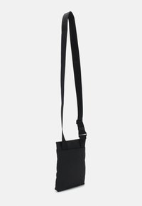 Borsa a tracolla nera con una texture di tessuto liscia, forma rettangolare, tracolla regolabile e design minimalista. Presenta una singola tasca frontale.