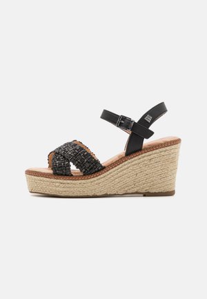 Sandalias de cuña trenzadas en negro con una suela de yute trenzado, con tiras cruzadas y una correa para el tobillo ajustable. Detalles en cuero suave.