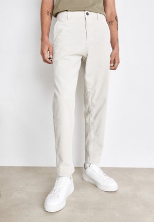 Pantaloni in velluto a coste color beige chiaro con taglio dritto, dotati di chiusura con bottone frontale e due tasche laterali, abbinati a sneaker bianche.