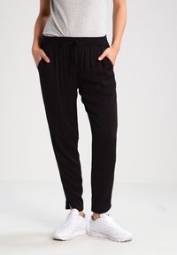 Černé joggingové kalhoty s elastickým pasem, bočními kapsami a zúženým střihem. Vybavené bílými teniskami a šedým topem.