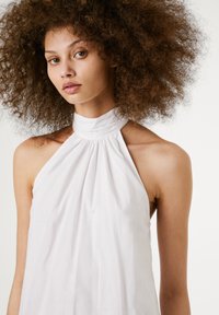 Top branco de halter com tecido franzido na gola, apresentando uma textura suave e um design sem mangas.