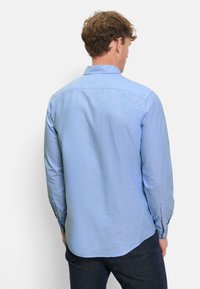 Camicia azzurro chiaro a maniche lunghe con colletto alla francese, polsini con bottoni e orlo curvo, realizzata in un tessuto morbido e strutturato.