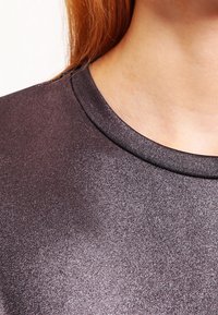 Czarna koszula o metalicznej teksturze z okrągłym dekoltem i gładkim materiałem, odbijająca światło z delikatnym efektem połysku.