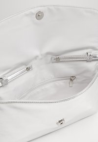 Intérieur de sac à main en cuir blanc avec matériel argenté. Comprend une poche à fermeture éclair et deux poches ouvertes pour l'organisation. Texture lisse.