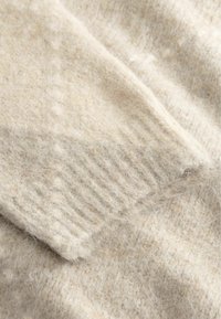 Μαλακό μπεζ μάλλινο μανίκι με ribbed τελείωμα που δείχνει μια χνουδωτή υφή πλεκτού υφάσματος κοντινή.
