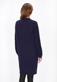 Abito lungo in maglia blu navy con colletto a girocollo a coste, maniche in maglia a treccia testurizzata decorate con piccole perline. Tessuto morbido e accogliente, vestibilità comoda.