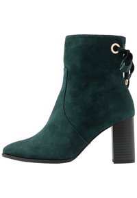 Stivaletto in suede verde con punta appuntita, accessori in oro e un nastro legato sul retro, caratterizzato da un tacco alto spesso e una suola testurizzata.