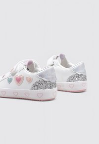 Zapatillas blancas con acentos en forma de corazón en rosa y azul. Presentan un talón plateado brillante y una suela rosa texturizada con patrones de corazones.