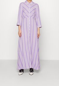 Dlouhé levandulové šaty s knoflíky, bílé zigzagové vzory, tříčtvrteční rukávy a límec; doplněné černobílými lodičkami.