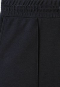 Pantaloni negri cu talie elastică, confecționați dintr-un material moale, având detalii cusute și plii pentru o textură și un design suplimentar.