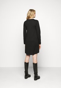 Abito nero a maniche lunghe con silhouette dritta, lungo fino a metà coscia e scollo dritto. Abbinato a stivali alti fino al ginocchio, lucidi e neri.