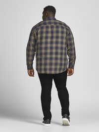 Plaid long-sleeve shirt in navy, yellow, and green; button-down collar; back yoke detailing; paired with black pants and dark sneakers.