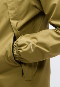 Αδιάβροχο μπουφάν σε ελιά πράσινο χρώμα με φερμουάρ σε τσέπη και ελαστικές μανσέτες, κατασκευασμένο από διαπνέον υλικό με την επωνυμία "DRYVENT".