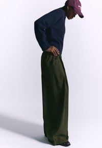 Navy sweater, loose-fitting olive wide-leg pants with pockets, and black slide sandals; textured material and relaxed design.