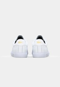 Baskets blanches avec tige en cuir lisse, bout arrondi, design profilé, accent de logo doré au talon et semelle en caoutchouc blanche.