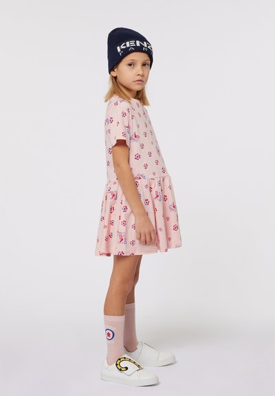 Robe à imprimé floral rose avec des manches courtes et une jupe froncée, associée à des chaussures slip-on blanches et des chaussettes rose clair. Bonnet bleu marine.